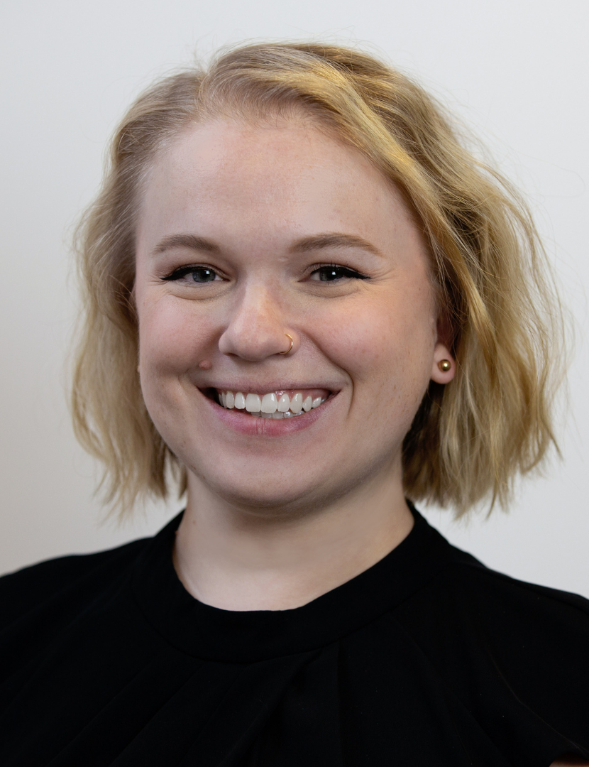 Headshot of Sarah Manteuffel smiling. Sarah has blonde wavy hair cut above the shoulders and is wearing a black shirt.